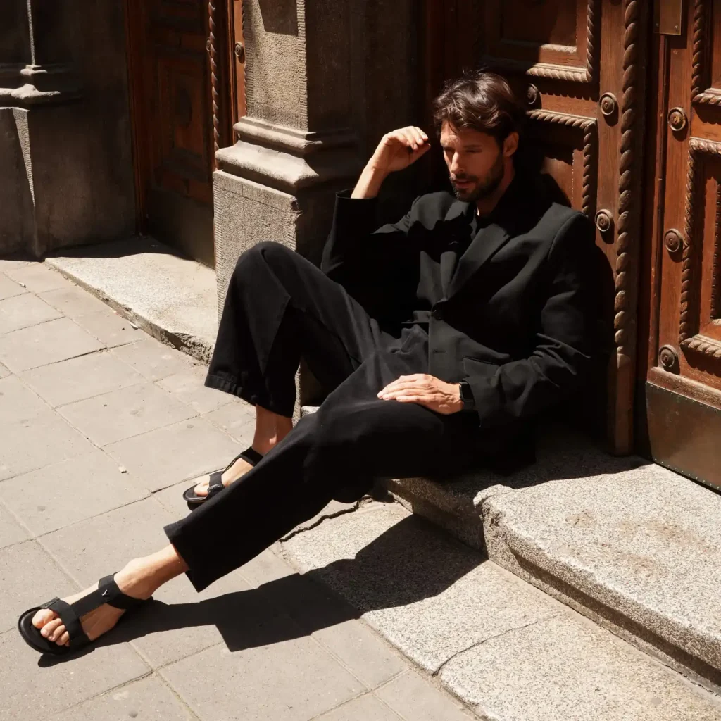 Elegantno obučen muškarac sedi na stepenicama u crnim yonso sandalama.